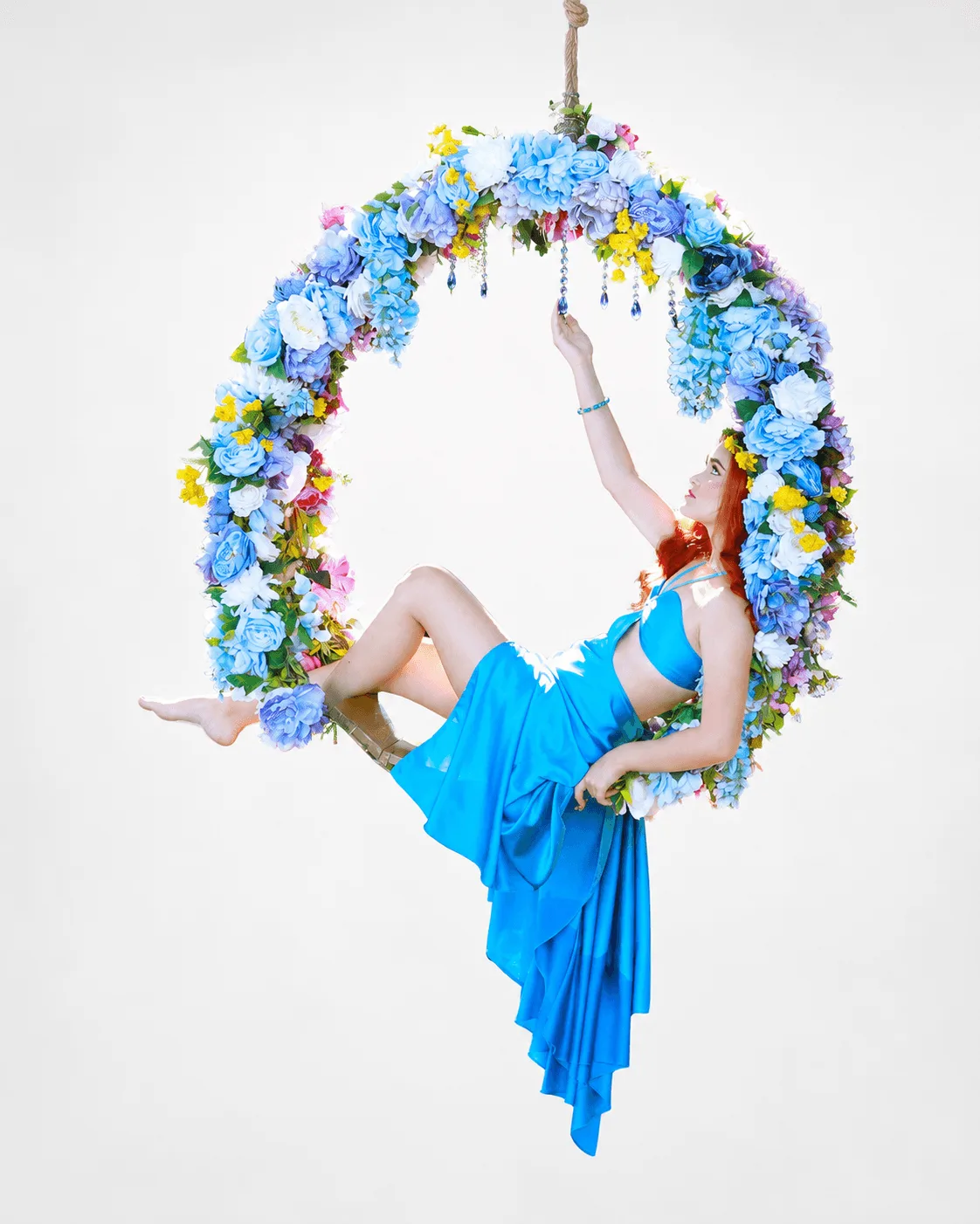 Quinceañera en un columpio de jardín decorado con flores blancas vistiendo un vestido azul rey