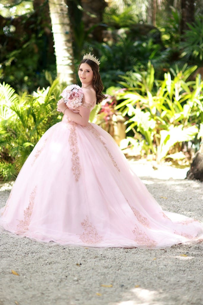 Quinceanera posing in a lush tropical garden with a pink princess dress