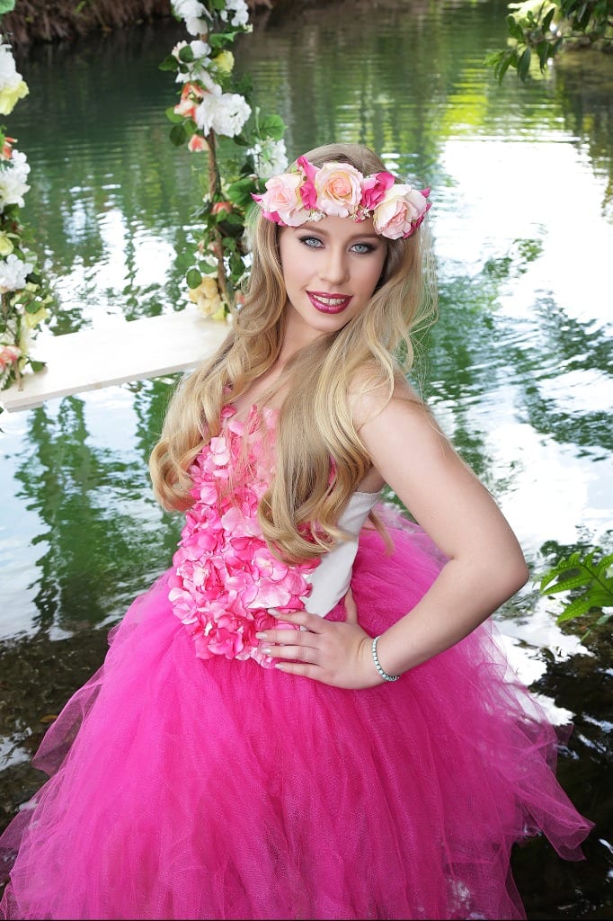 Quinceanera sitting on a flower-wrapped swing wearing a pink gown in Secret Gardens Miami