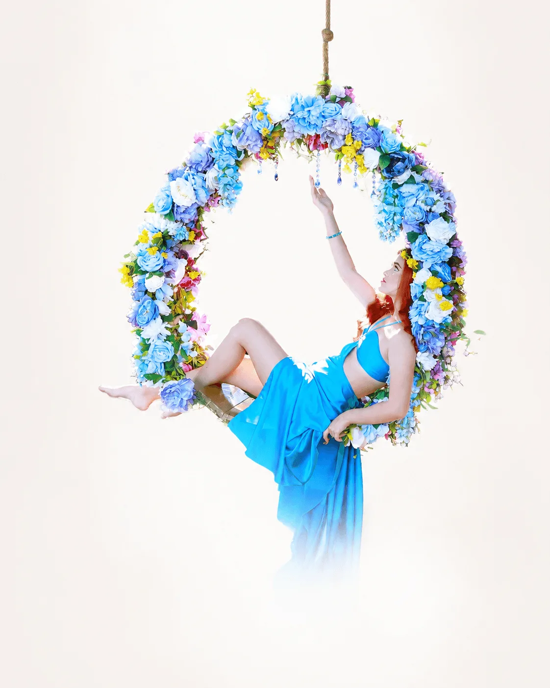 Quinceanera posing on a floral swing wearing a royal blue gown in a lush garden