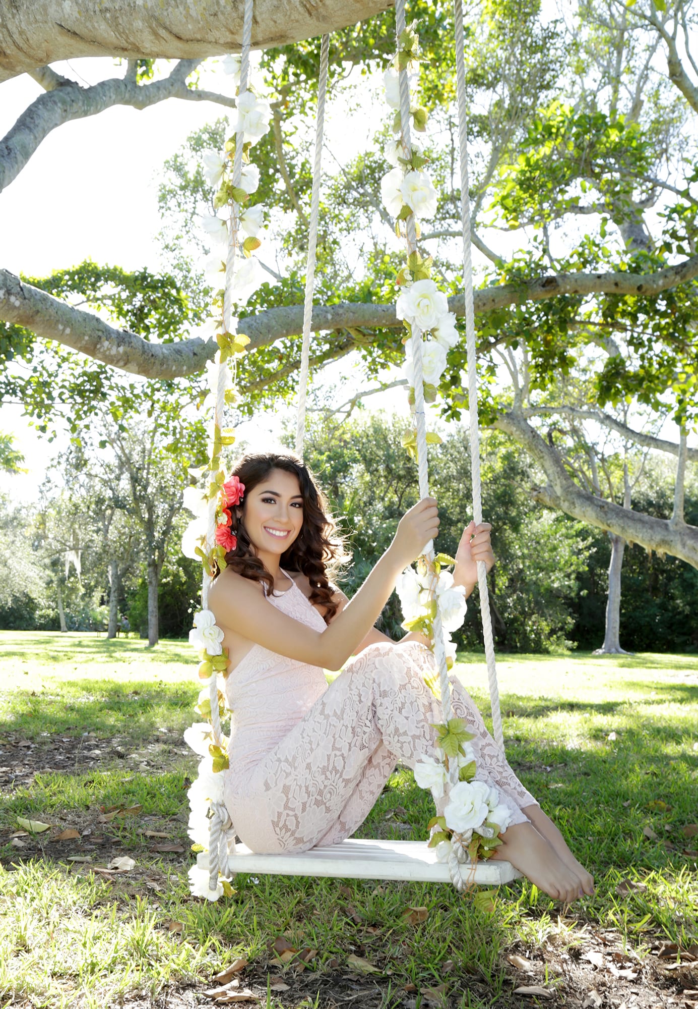 Quinceanera smiling on a classic swing wearing a vibrant yellow dress in a forest park